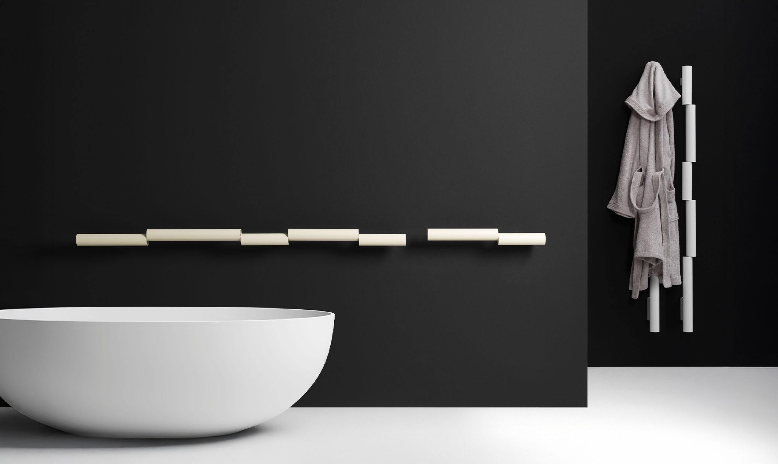 Radiateur Pypeline crème posé à l'horizontale sur un mur noir, version verticale blanche avec peignoir, baignoire blanche