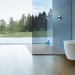 WC lavant Duravit suspendu blanc contre un mur gris bleu, parquet clair et baie vitrée ouverte sur la forêt